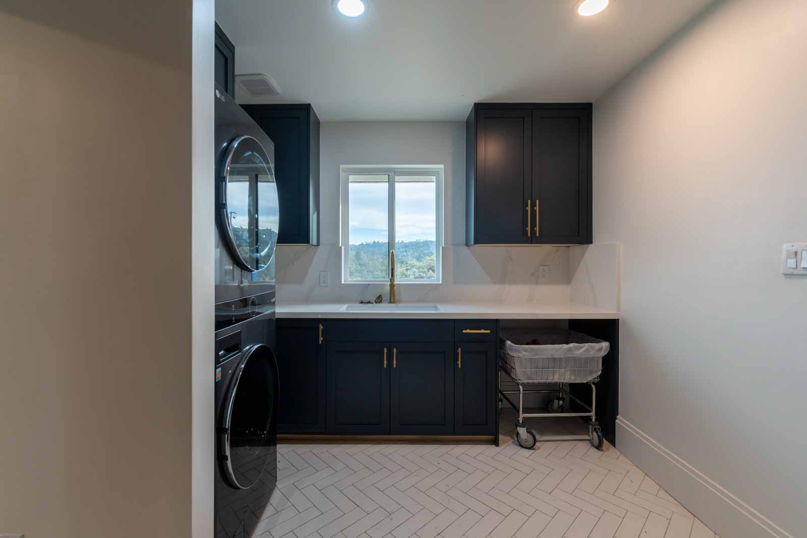 Herringbone tile laundry room with navy cabinets and gold hardware