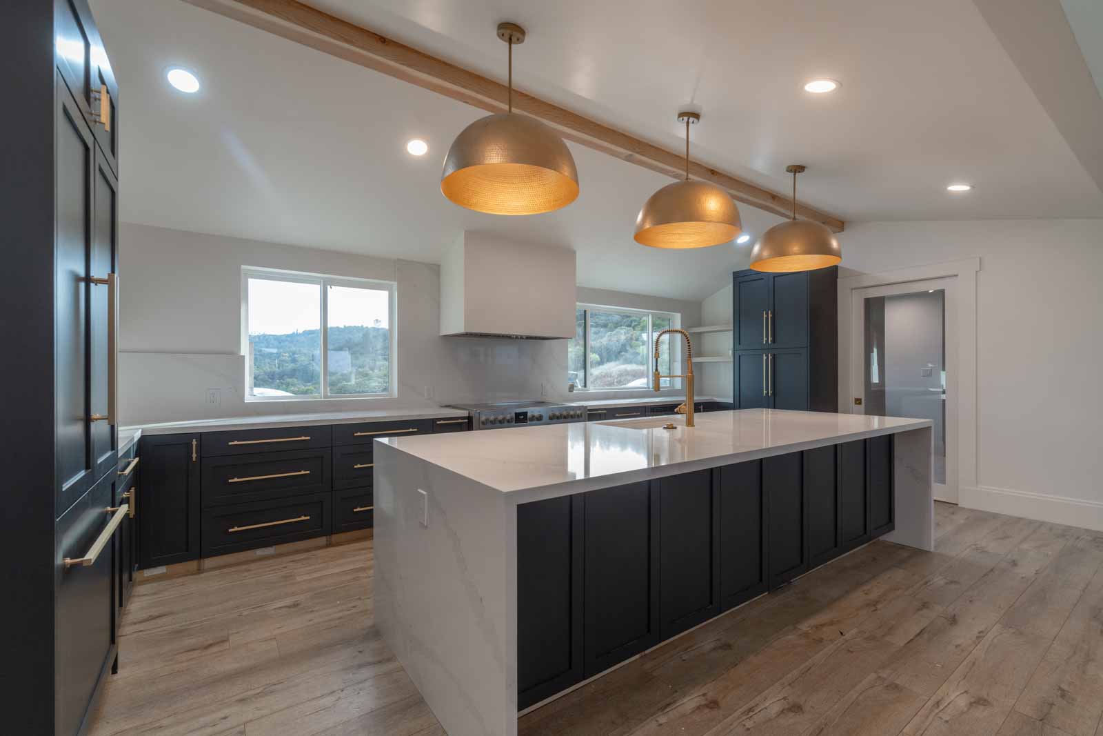 Navy kitchen with wood beam ceiling, gold pendants, and professional range