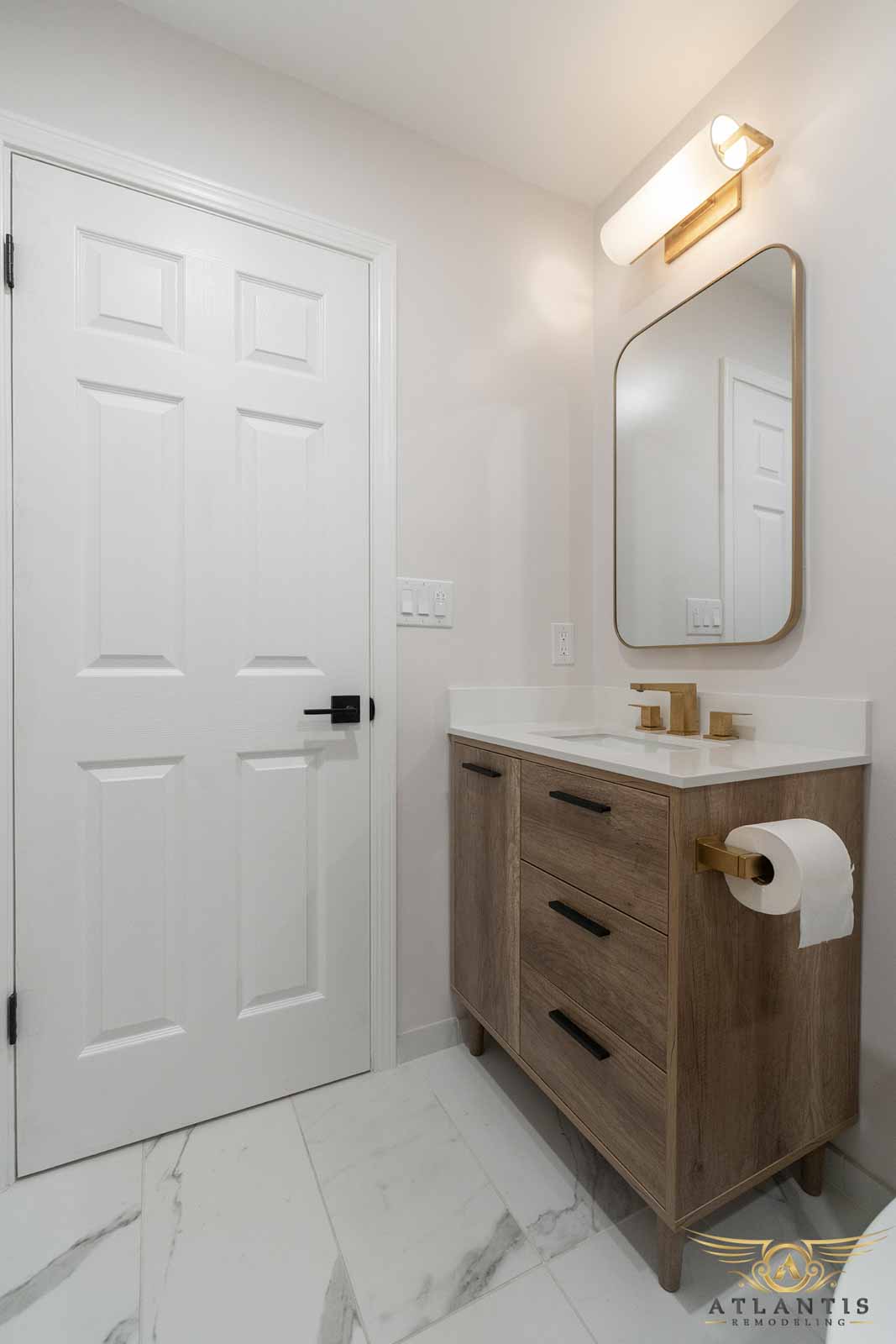 Powder room with oak vanity, gold faucet, rounded mirror, and marble floor