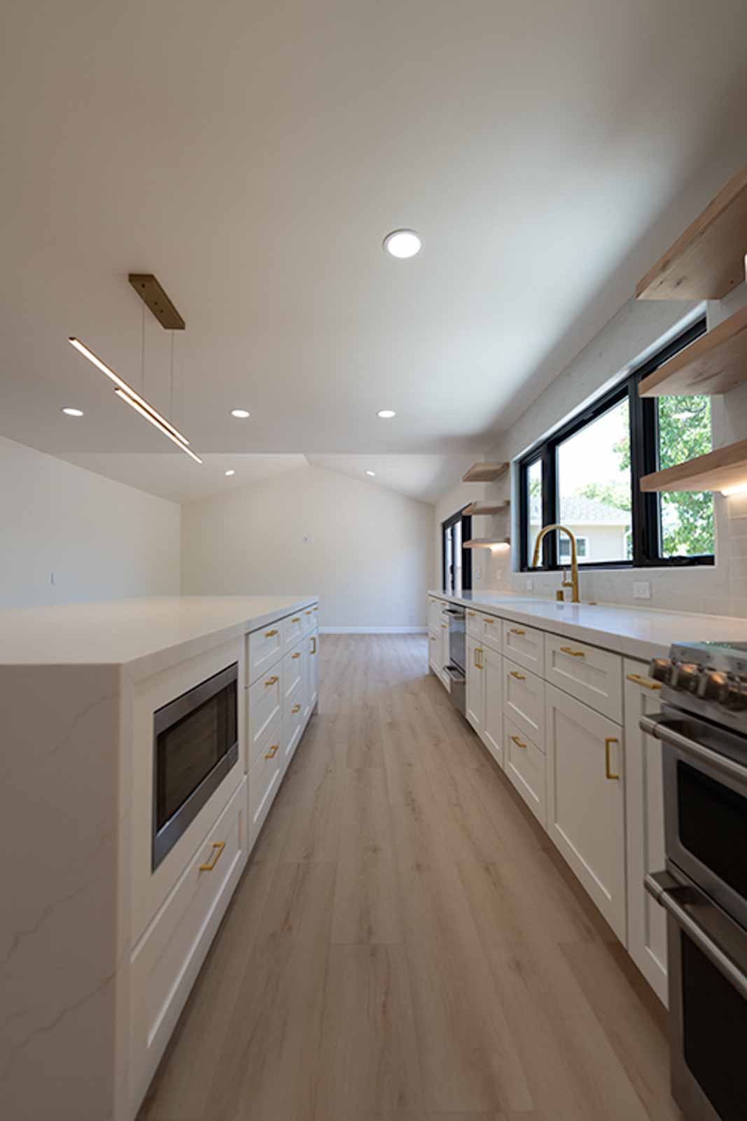 Galley kitchen with white cabinets, gold hardware, built-in microwave island, and linear pendant