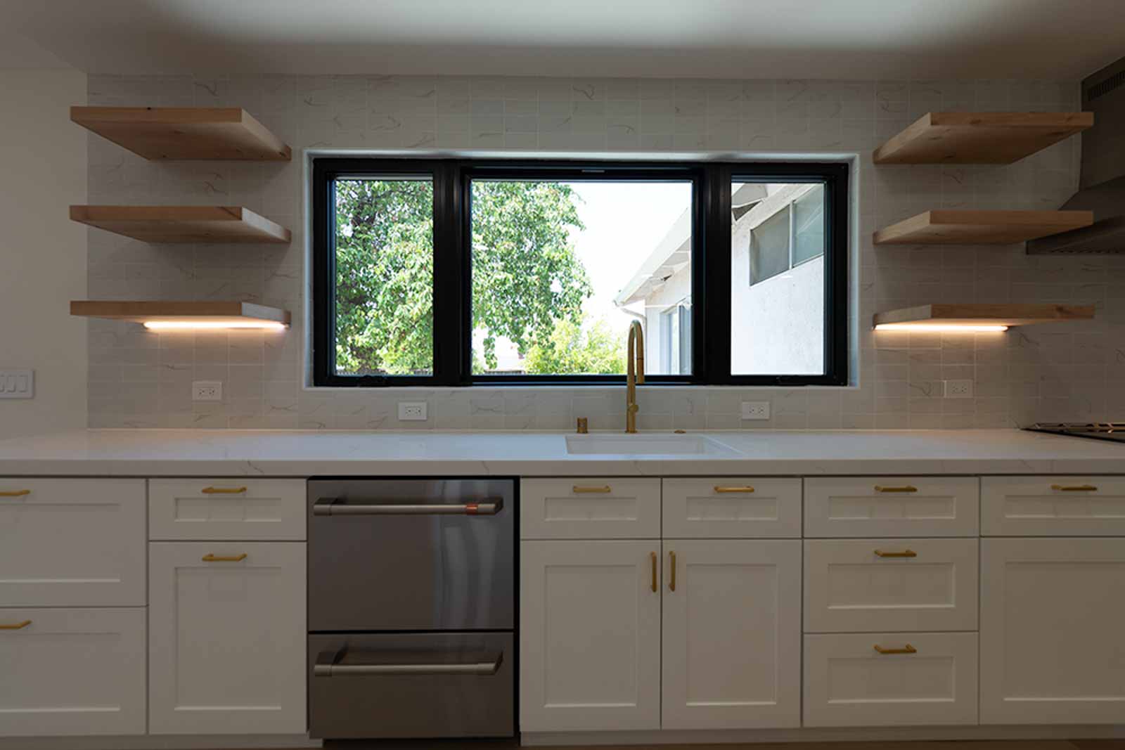 Gold faucet sink detail with floating wood shelves, black-framed window, and marble backsplash