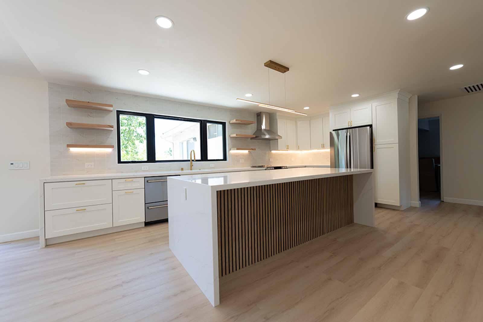 Open kitchen with quartz waterfall island, wood slat panel, floating shelves, and stainless fridge